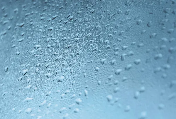 Su damlacıklarıyla kaplı bir yüzeye yakın çekim. Damlacıkların boyutları değişiyor ve ferahlık ve nem hissi veren dokulu ve serin tonlu bir desen yaratıyorlar..