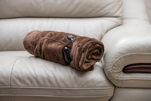 rolled up electric blanket with portable charger as a power supply on a sofa