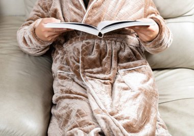 Evcil, tüylü kışlık ceketli ve kanepede kitap okuyan bir adam.