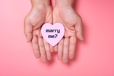 man holding a heart shape paper written with marry me