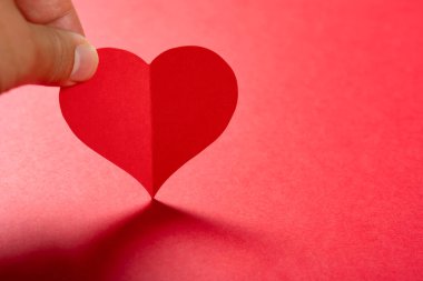 Kırmızı arka planda kalbi tutan parmaklar.