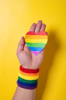 man with LGBT rainbow wrist band and paper heart at vertical composition