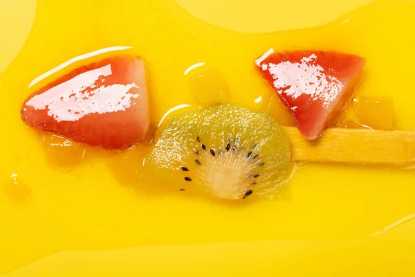 top view yellow peach flavor with kiwi and strawberry slices popsicle melted on yellow background