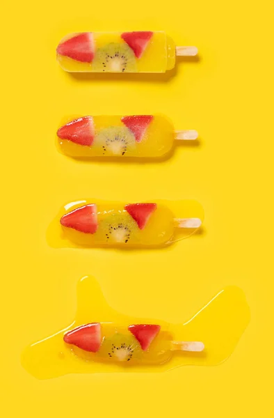yellow peach flavor with kiwi and strawberry slices popsicle melting process on yellow background at vertical composition