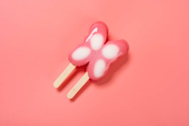 Üst manzara kelebek şekilli buzlu çubuk pembe arka planda erimeye başlar