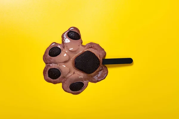 top view bears paw shape chocolate flavor popsicle in a melting process on yellow background