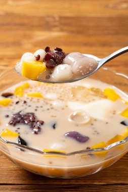 Çimen jölesi, mango, şeftali sakızı, tapyoka, kırmızı fasulye ve jöle karışımı bir kase süt şurubu yemek. dikey bileşiminde