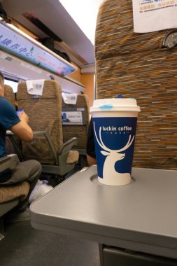 GUILIN GUANGXI Çin-14 Temmuz 2024: Dikey kompozisyonda bir yüksek hızlı trende bir masanın üzerinde bir fincan şanslı kahve.