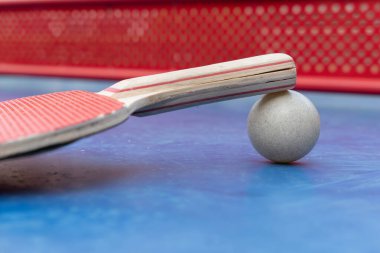 yatay kompozisyonda mavi bir pingpong masasında pingpong raketi, top ve net açısı