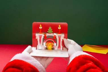 Noel Baba elinde Noel süslemeleri sobasıyla 3 boyutlu bir hediye kartı tutuyor.