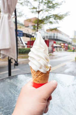 El ele tutuşan dondurma külahı açık havada dikey kompozisyonda.
