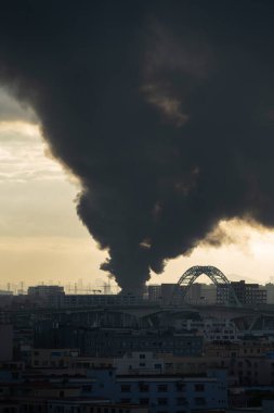 Sabahın erken saatlerinde yanan uzak bir kasaba dikey bileşimde yoğun siyah duman yayıyor.