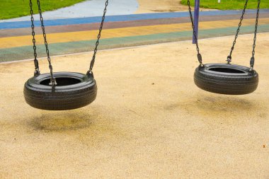 Renkli bir parkta sessizce asılı duran iki lastik salıncağı.