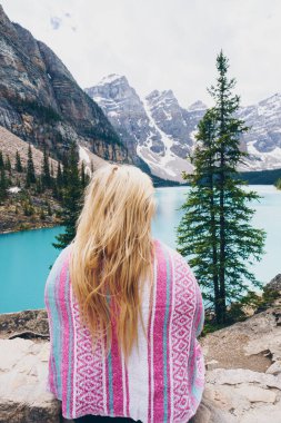 Sarışın bir kadının pembe bir battaniyeyle sarılıp Kanada 'daki Moranie Gölü' ne bakışının arkası.