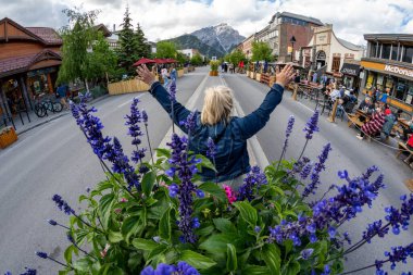 Banff, Alberta, Kanada - 10 Temmuz 2022: Banff Ulusal Parkı 'ndaki ünlü Banff Caddesi' nin Fisheye manzarası - kadın turist kollarını açmış poz veriyor