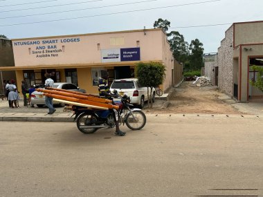 Ntungamo, Uganda, Afrika - 25 Mart 2023: Tipik bir yol kenarı pazarı sahnesi, bir adamın motosikletli bir boda üzerinde yatak çerçevesi taşıması gibi