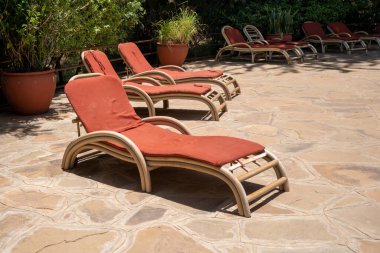 Havuz şezlongları bir tatil köyünün verandasında güneşleniyor.
