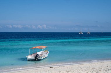 Zanzibar, Tanzanya - 16 Mart 2023: Plaja yakın kristal berrak turkuaz suda küçük bir tekne yanaştı