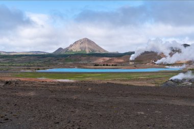 Kuzey İzlanda 'nın Myvatn bölgesinin manzarası, jeotermal enerji santrali ve mavi sülfürik göl, arka planda dağlar.