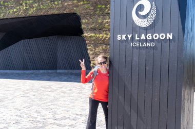 Kopavogur, İzlanda - 11 Temmuz 2023: Sky Lagoon Spa - giriş tabelasının yanında mutlu bir turist kadın poz verdi