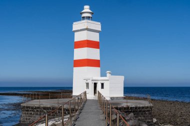 İzlanda 'daki Gardur Old Lighthouse, güneşli bir günde beyaz ve kırmızı çizgili bir deniz feneri