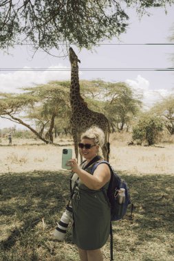 Naivasha Gölü - yürüyen safariye çıkan turist kadın, vahşi bir zürafayla yemek yerken selfie çeker.