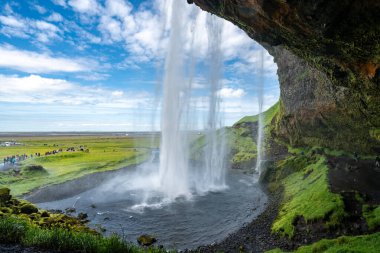 Seljalandsfoss Şelalesi, güneşli bir günde İzlanda 'da şelalenin arkasından yürümekten manzara