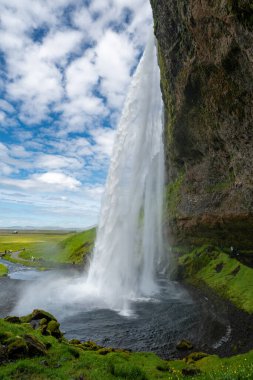 Seljalandsfoss Şelalesi, güneşli bir günde İzlanda 'da şelalenin arkasından yürümekten manzara