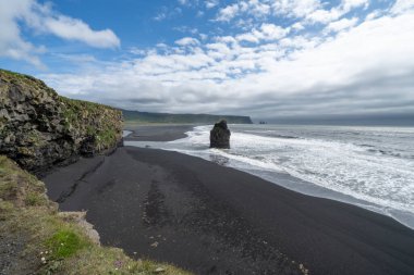 İzlanda 'daki Dyrholaey bölgesinde deniz yığınları ve siyah kumsal var.
