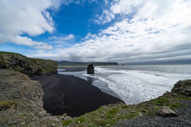 İzlanda 'daki Dyrholaey bölgesinde deniz yığınları ve siyah kumsal var.