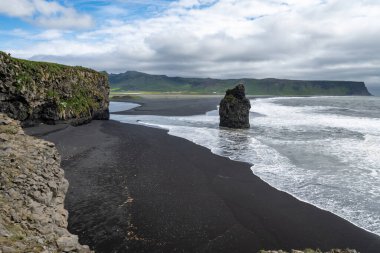 İzlanda 'daki Dyrholaey bölgesinde deniz yığınları ve siyah kumsal var.