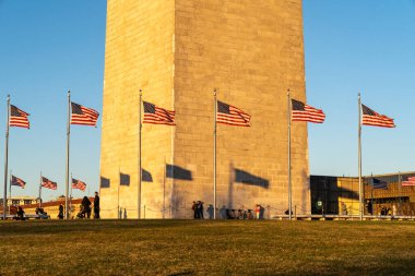 Washington, DC - 19 Kasım 2023: Turistler ziyareti sırasında Washington Anıtı. Gölgeler veren bayraklar