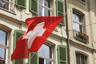 Bern İsviçre 'de çekilen sevimli pencere ve panjurların yanında rüzgarda dalgalanan İsviçre bayrağı.