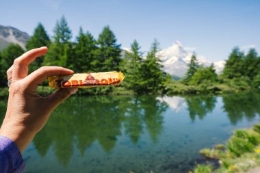 Zermatt, Switzerland - July 27, 2024: Hand holds a Tobelrone chocolate candy bar in front of Grindjisee lake located on the Five Lakes hike. Matterhorn Peak visible clipart