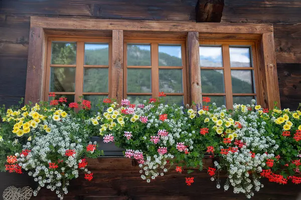 stock image Picturesque chalet window with red flowers in flower box in Zermatt, Switzerland, during summertime