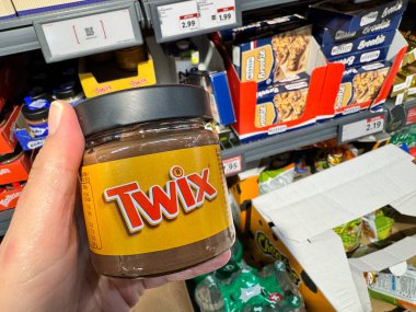 Basel, Switzerland - December 9, 2024: Hand holds a jar of Twix nut butter spread at a Lidl grocery store clipart