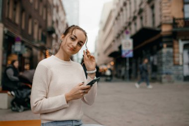 Varşova 'da sokakta duran akıllı bir telefon kullanan, süveterli, şık bir kadın..