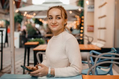 Varşova 'da sokakta duran akıllı bir telefon kullanan, süveterli, şık bir kadın..