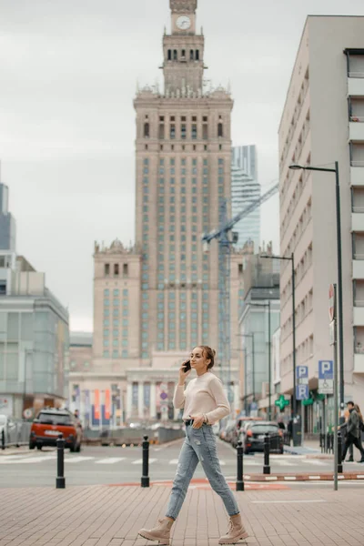 stock image Young woman using mobile phone walking on the city street in Warsaw, Poland.