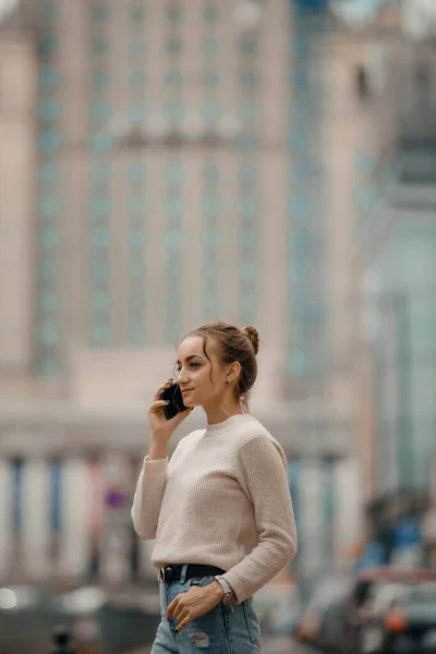 Young woman using mobile phone walking on the city street in Warsaw, Poland.