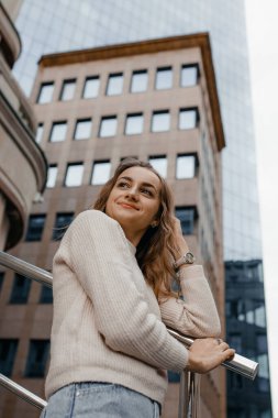 Profesyonel kadın işçiler açık havada duran teraslı takım elbise giyer. Parmaklıklara yaslanmış büyük bir gülümsemeyle modern ofis gökdeleninin keyfini çıkarırlar..