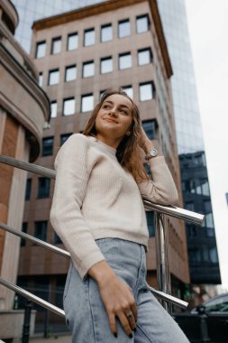 Profesyonel kadın işçiler açık havada duran teraslı takım elbise giyer. Parmaklıklara yaslanmış büyük bir gülümsemeyle modern ofis gökdeleninin keyfini çıkarırlar..