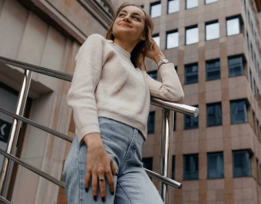 Profesyonel kadın işçiler açık havada duran teraslı takım elbise giyer. Parmaklıklara yaslanmış büyük bir gülümsemeyle modern ofis gökdeleninin keyfini çıkarırlar..
