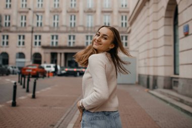 Şehrin arka planında bej kazaklı, gülen esmer kızın yakın plan portresi..