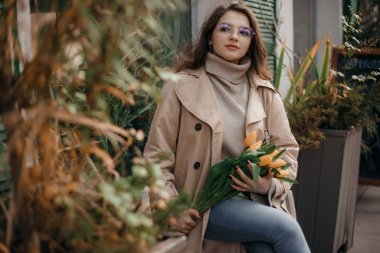 Bir buket lale içinde güzel bir kadın. Moda sokak fotoğrafçılığı. Sarı laleli genç mutlu kız park hayatı fotoğrafında yürüyor..