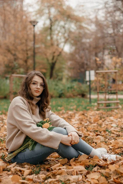 外面的照片是快乐的年轻女士在秋天的公园里玩乐的照片 在秋天的公园里 一个年轻的女人带着一束郁金香 秋天的时间 — 图库照片