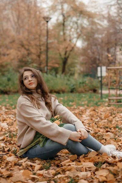 外面的照片是快乐的年轻女士在秋天的公园里玩乐的照片 在秋天的公园里 一个年轻的女人带着一束郁金香 秋天的时间 — 图库照片