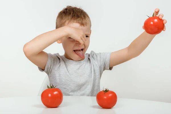 The boy don\'t like tomato. Nutrition and healthy eating habits for kids concept. Children do not like to eat red tomatoes. Little cute kid, boy refuse to eat healthy vegetables.