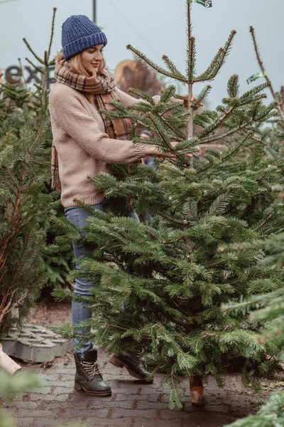 エレガントな女の子はクリスマスツリーを購入します 女性の青いキャップとスカーフ 金髪の美しい女性 クリスマスの時間 — ストック写真