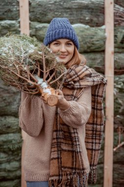 Mavi şapkalı güzel bir kız, atkısı omuzunda bir Noel ağacı taşıyor. Noel 'de giyinmiş bir kız Noel' de süslemek için yeni kesilmiş bir köknar ağacı getiriyor. Yeşil konsepti koru.